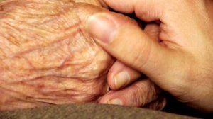 stock-footage-senior-old-woman-young-man-hold-hand-wrinkle-skin-close-up